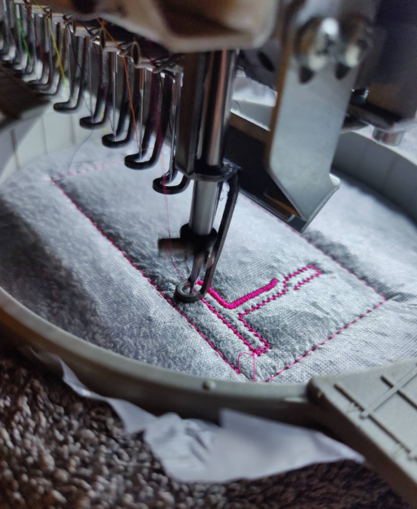 A close up of the embroidery machine adding a pink letter T to a towel. 