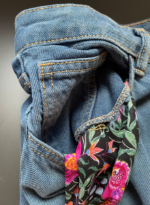 A pair of jeans with its pocket turned out to reveal colourful fabric. The pocket enlarges the original jeans pocket.